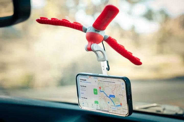 Smartphone displaying navigation directions, held horizontally by a red suction tripod on a car windshield.
