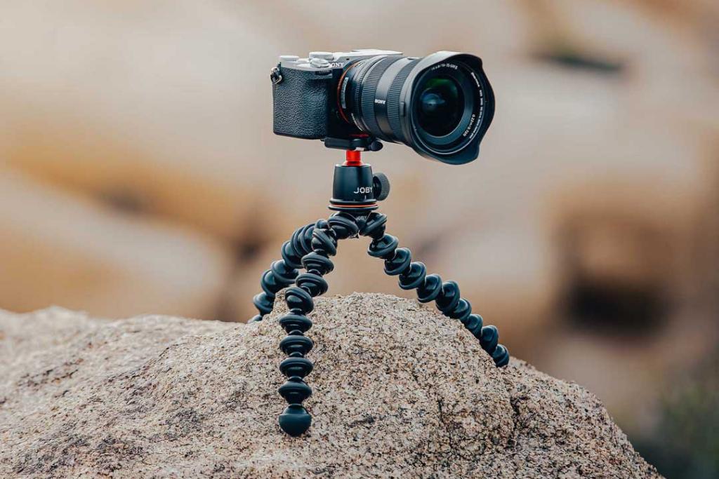 JOBY GorillaPod flexible tripod supporting a mirrorless camera with its legs spread across an uneven rock.